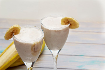 Homemade Banana smoothies or coctail on wood table in two glasses decorated with piece of banana