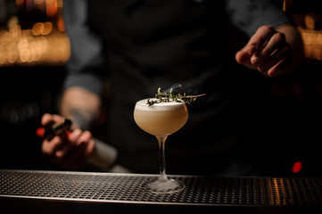 Bartender adds rosemary in alcohol light brown cocktail