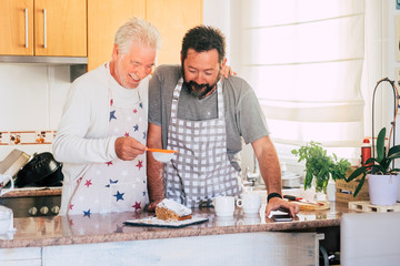 Caucasian couple at home preparing a cake together - father and son adult and senior working in the kitchen - cooking men chef at work with joy and happiness