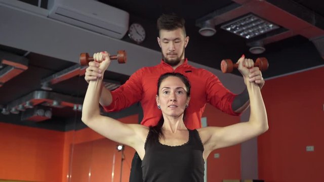 Young healthy sporty active shape girl with a handsome helpful personal trainer next to her in the gym. Sport activity