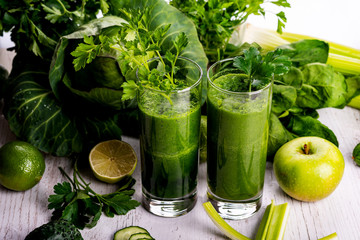 Green smoothie with fruits and vegetables on white wooden background.