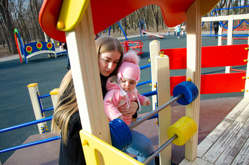 Mom plays on a bright playground with a small child in the street, nomads, a house during the day