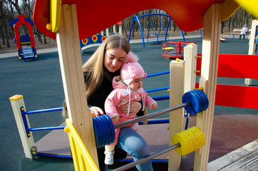 Mom plays on a bright playground with a small child in the street, nomads, a house during the day