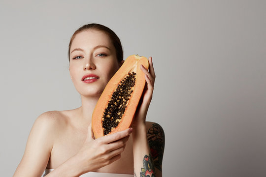 Beauty female model holding juicy papaya slice. Beautiful Joyful teen girl with freckles, funny red hairstyle and brown makeup. dvertisement and health lifestyle. Isolated on white background.