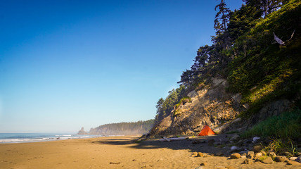 Orange tent at the expansive beach by wooded cliff side in the morning.