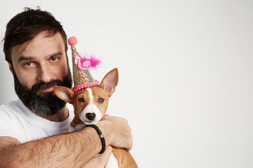 Attractive bearded man hugging his basenji puppy dog, happy birthday baby dog, against a white background. Copy paste space mock-up