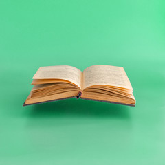 Levitating open old book on green background.  Minimal concept.
