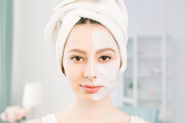 an attractive young girl with a white towel on her head applied a useful clay mask to half the face