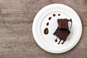 Homemade brownie served with chocolate fudge. Sweet dessert on wooden background.