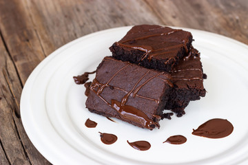 Homemade brownie served with chocolate fudge. Sweet dessert on wooden background.