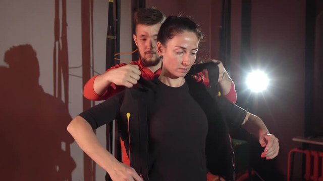EMS electro stimulation sports equipment in gym. Trainer and woman doing exercises