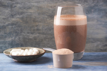 Glass of Chocolate Protein Shake with milk and banana. Whey protein in scoop and BCAA amino acids in background. Sport nutrition. Wooden background. Copy space. 