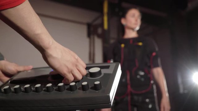EMS electro stimulation sports equipment in gym. Trainer and woman doing exercises