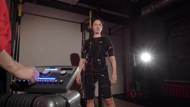 EMS electro stimulation sports equipment in gym. Trainer and woman doing exercises