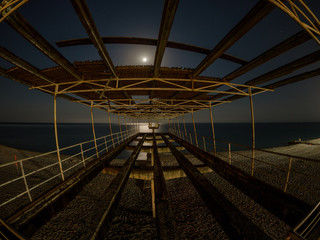 Old concrete pier on the beach at night in the moonlight.