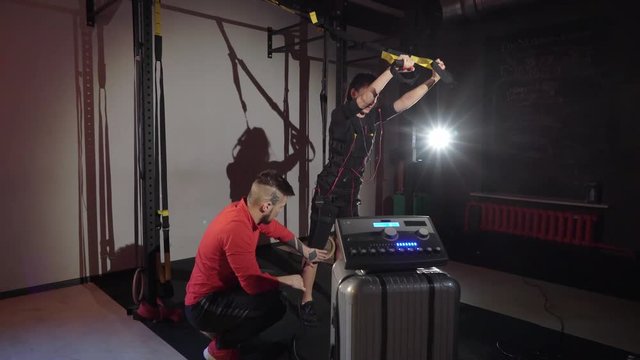 EMS electro stimulation sports equipment in gym. Trainer and woman doing exercises