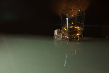 Whisky glass cold ice cube in the shape of a skull  accompanied by a bottle elegantly reflecting the composition in a glass base to de world in Mexico