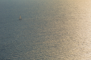 Seascape with small sailing boat with stretched sails. Beautiful sunset, sun reflecting in sea waves, boat in sunlit. Creative view from above.