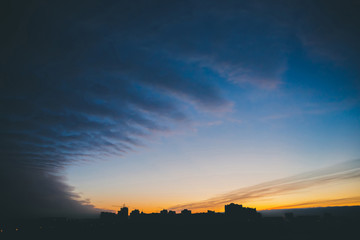 Cityscape with wonderful varicolored vivid dawn. Amazing dramatic blue cloud sky above dark...