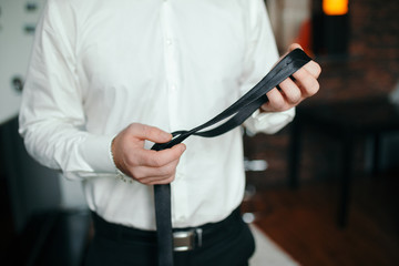 People, business,fashion and clothing concept - close up of man in shirt dressing up and adjusting tie on neck at home.