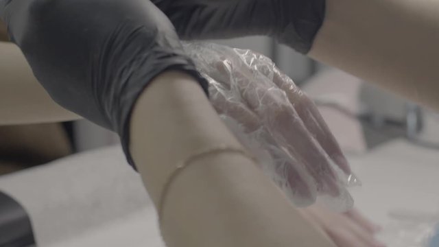 Manicurist in black latex gloves aligns the cream under a disposable cellophane glove on the client's right hand in the beauty salon. Brazilian manicure. Ultra HD. 4K, 3840x2160. 25 FPS