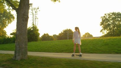 Golden evening sunbeams shine on the happy Caucasian woman riding her skateboard
