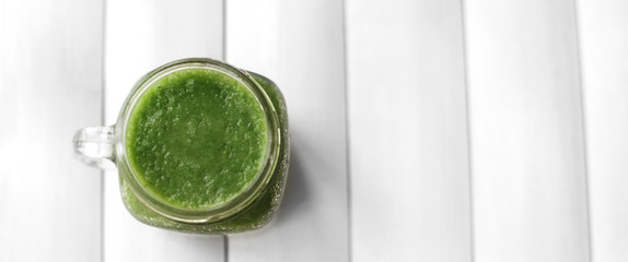 Green smoothie in glass mason jar on white wooden table on white background. Place for text. top view