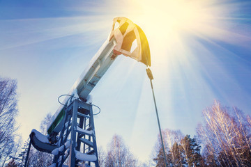 Oil field with pump jack, profiled on blue sky with white clouds, on a sunny day in spring