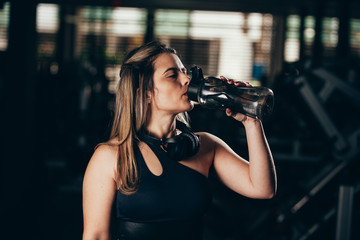 A young woman taking a break at the gym with a bottle of water or energy drink