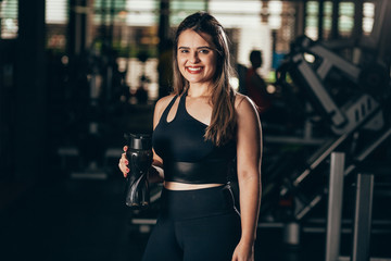 A young woman taking a break at the gym with a bottle of water or energy drink