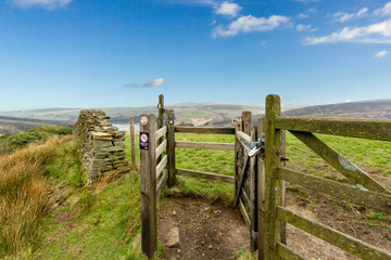 Fototapeta na wymiar A view of a wooden walker gate with green vegetation, lake and hills in the background under a majestic blue sky and white clouds