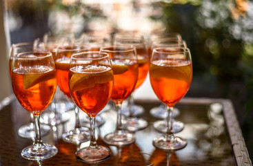 Aperol spritz cocktails on glass table with reflections and blurry background.