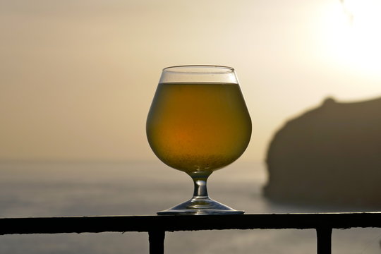 A glass of poncha at sunset on Madeira with stunning views of the rocky coastline. Poncha is a traditional alcoholic beverage from the island of Madeira