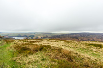 A view of a lake in a valley with green grass slopes under a white cloudy sky