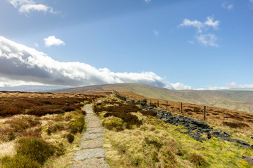Fototapeta premium A view of a stony path trail along heater in the hill under a majestic blue sky and white clouds