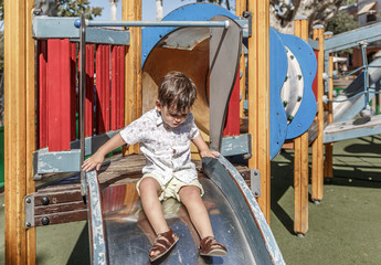 Fototapeta na wymiar A cute blond toddler glides happily down a slide of a nice park