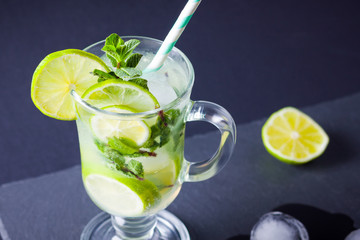 Mojito with ice on black background. Mojito cocktail with lime and fresh mint on slate board. Summer refreshing cocktail with citrus and ice on dark background