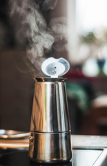 Atmospheric warm photo of a coffee maker on a stove with boiling coffee and steaming steam on a blurry background