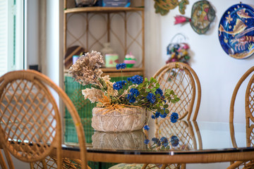 Dining room with big glass table and decorations all around the place. Dried flowers, wicker chairs, clay pottery. Cozy atmosphere at home. concept of waiting dinner time. Bright sunlight from windows