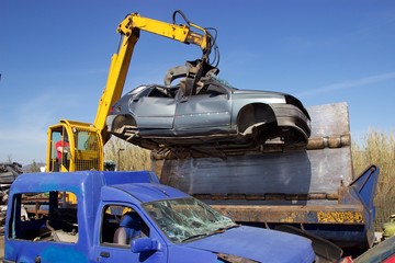 Crane with claw move an old crushed car from junkyard at car press crusher for recycling 