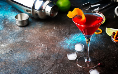 Classic alcoholic cocktail cosmopolitan with vodka, liqueur, cranberry juice, lime, ice and orange zest, dark bar counter background, night mood, space for text - obrazy, fototapety, plakaty