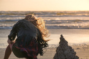 Young woman building and making sand castle next to sea. Calm, relaxing and romantic evening during...