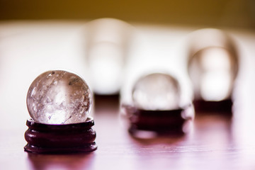 Fortune telling. A macro shot of a glass ball on a wooden pad, with sun reflections, bubbles and a rainbow in it, standing on a pine dining table in the middle of a kitchen.  