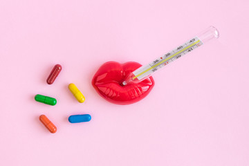 Thermometer in plastic lips and multicolored pills medicine abstract.