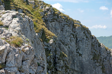 Fototapeta premium Sunny summer day at mountain peak, where tourists climb to conquer fear, find courage and develop lateral thinking skills to overcome difficulty of climbing a mountain. Small road with rolling stones 