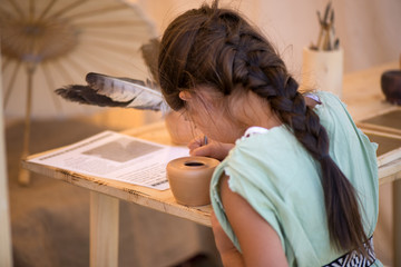 Fototapeta na wymiar Young girl is writing with old quill pen on the old paper. Historical atmosphere. Writing calligraphy on reenactment festival in summer in Romania. 