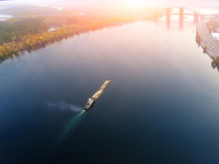 Scenic aerial cityscape of Kiev and river Dnipro at sunset. Tugboat supporting barge with sand bulk materials heading down river Dnieper. Ukrainian inland navigation and river freight cargo - obrazy, fototapety, plakaty
