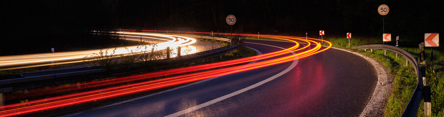 Lichtspur auf der Autobahn mit Tempo 50 Schildern in einer steilen Kurve.