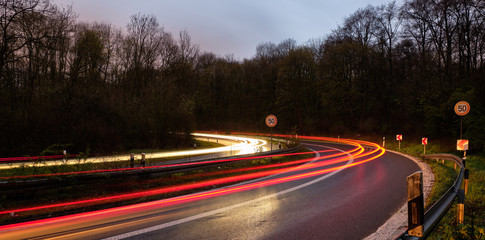 Lichtspur auf der Autobahn mit Tempo 50 Schildern in einer steilen Kurve.
