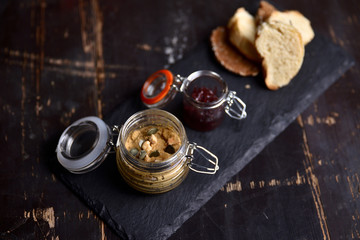 liver pate with nuts and croutons in a glass jar on a dark background